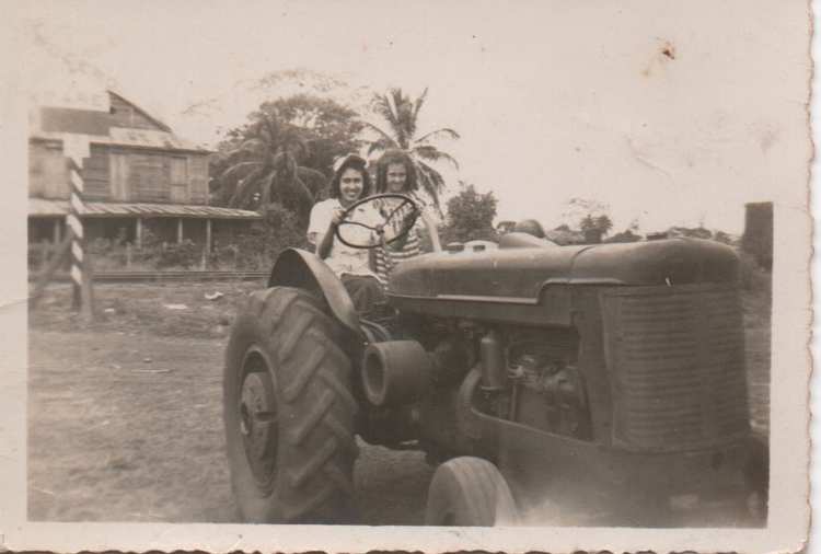 Flérida frente al volante de un tractor. Al fondo, luego de la señalización del crucero Ferroviario, una vista del Bar de Irimía.